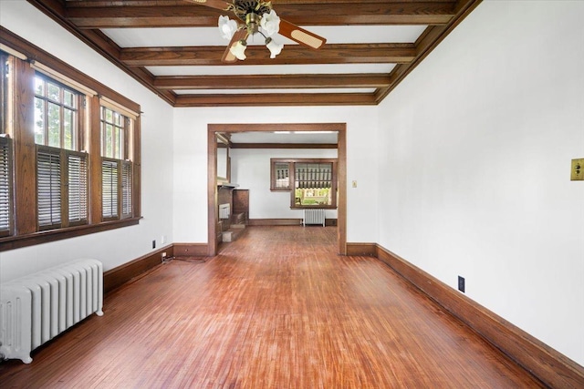 empty room with radiator heating unit, wood finished floors, beam ceiling, baseboards, and a ceiling fan