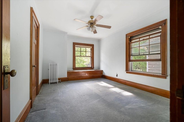carpeted spare room with radiator, baseboards, crown molding, and a ceiling fan