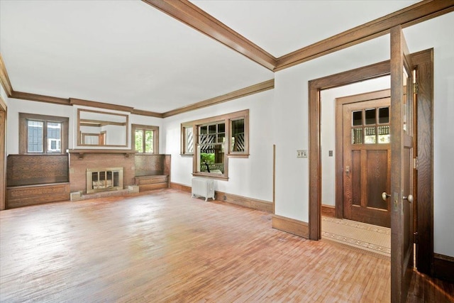unfurnished living room featuring crown molding, light wood-style floors, radiator heating unit, a fireplace, and baseboards