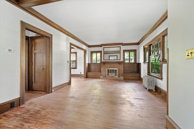 unfurnished living room featuring radiator heating unit, light wood-style floors, ornamental molding, a brick fireplace, and baseboards