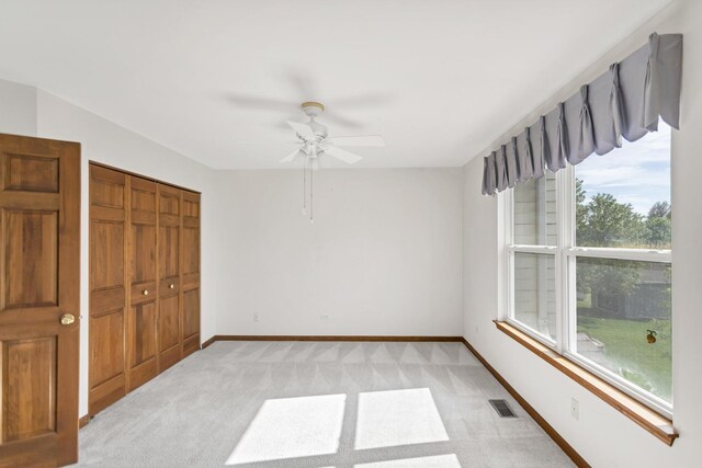 unfurnished bedroom featuring light carpet, a closet, baseboards, and ceiling fan