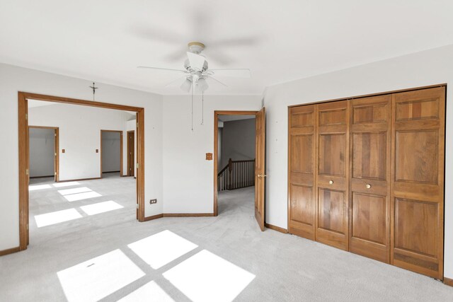 unfurnished bedroom with light carpet, baseboards, a ceiling fan, and a closet