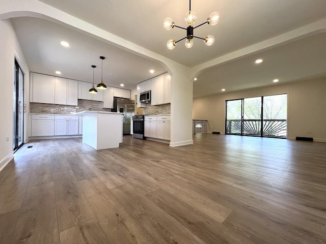 kitchen with open floor plan, stainless steel appliances, arched walkways, a chandelier, and recessed lighting