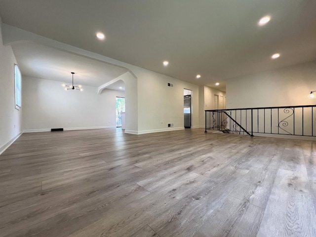 unfurnished room with wood finished floors, recessed lighting, a chandelier, baseboards, and arched walkways