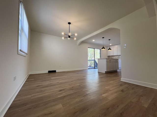 unfurnished living room featuring arched walkways, dark wood finished floors, a chandelier, baseboards, and recessed lighting