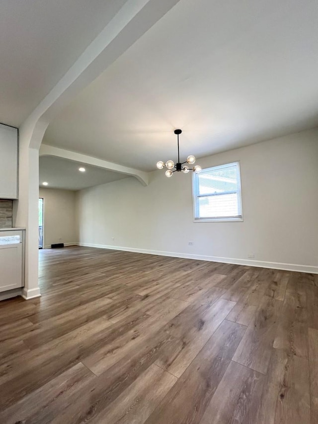 unfurnished dining area with dark wood finished floors, a chandelier, arched walkways, baseboards, and recessed lighting