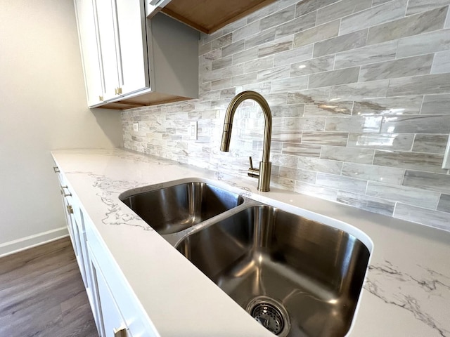kitchen view of a sink, backsplash, white cabinetry, light stone counters, and baseboards
