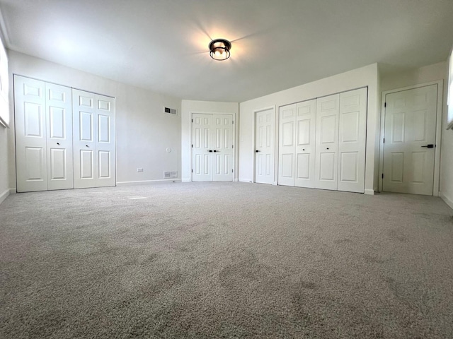 unfurnished bedroom with two closets, baseboards, and carpet flooring