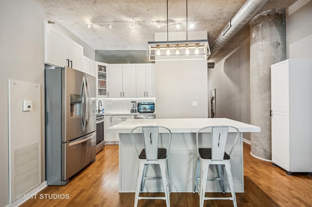 700 N Larrabee St Unit 905, Chicago, IL 60654 - kitchen with appliances with stainless steel finishes, light countertops, wood finished floors, a kitchen island, and glass insert cabinets