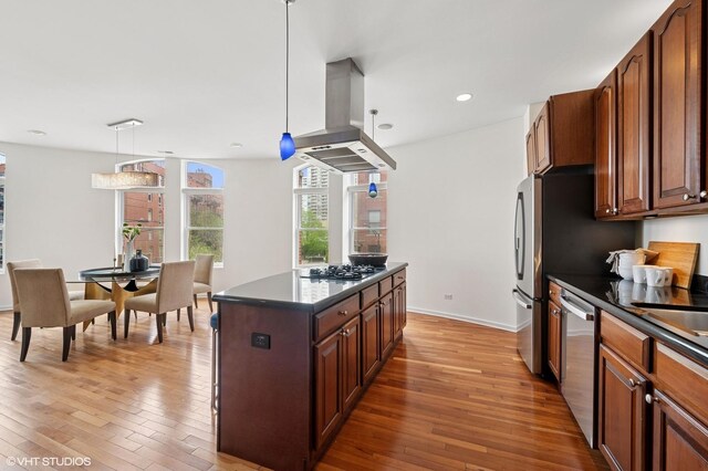 501 N Kingsbury St Unit G, Chicago, IL 60654 - kitchen with island exhaust hood, stainless steel appliances, dark countertops, light wood-style floors, and recessed lighting