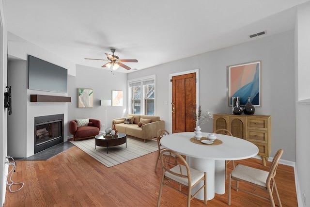 dining area featuring ceiling fan, a fireplace with flush hearth, and wood finished floors