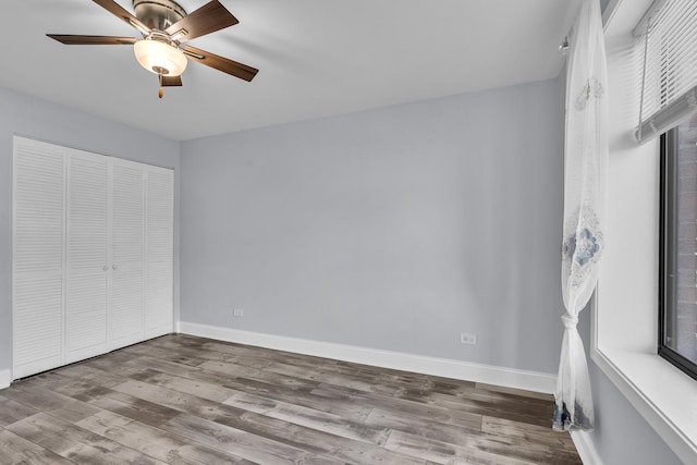 unfurnished bedroom featuring wood finished floors, baseboards, a closet, and ceiling fan