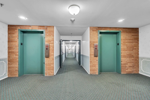 hall with carpet, elevator, and brick wall