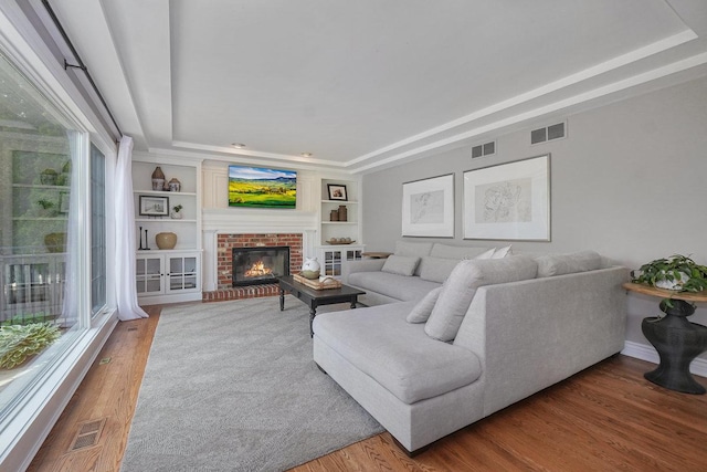 living room with a tray ceiling, wood finished floors, a fireplace, built in shelves, and baseboards