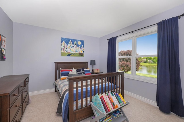 bedroom featuring light colored carpet, baseboards, and a water view