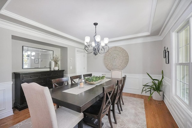 dining space with a chandelier, light wood-style flooring, crown molding, and a wainscoted wall
