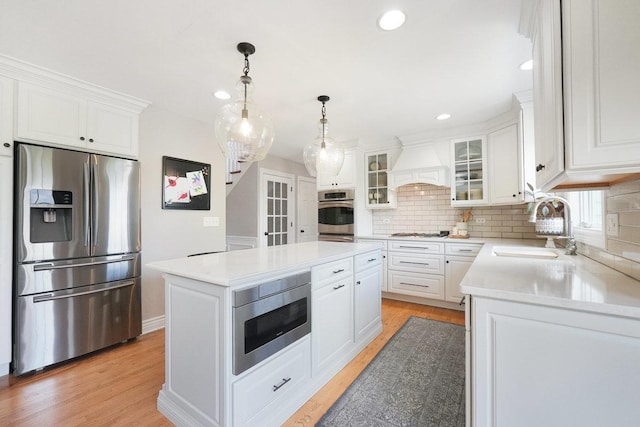 kitchen with appliances with stainless steel finishes, a sink, premium range hood, tasteful backsplash, and white cabinetry