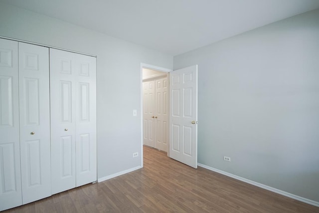 unfurnished bedroom featuring baseboards, wood finished floors, and a closet