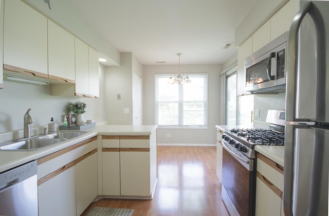 kitchen featuring appliances with stainless steel finishes, a sink, a peninsula, light wood-style flooring, and light countertops