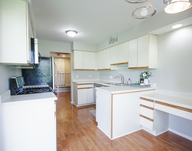 kitchen with a sink, appliances with stainless steel finishes, a peninsula, light wood finished floors, and light countertops