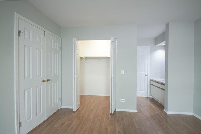 unfurnished bedroom featuring dark wood-style floors, a spacious closet, a closet, and baseboards