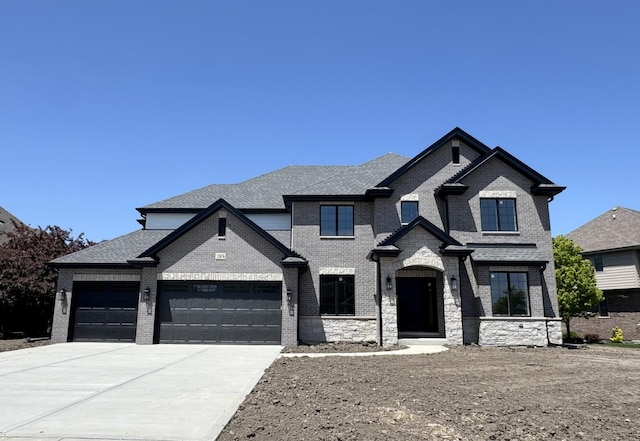 french country style house featuring concrete driveway, a garage, brick siding, a shingled roof, and stone siding