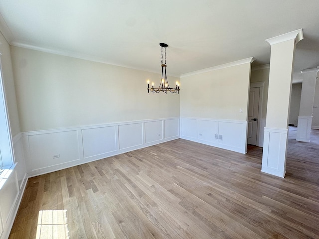 unfurnished dining area with ornamental molding, wood finished floors, a decorative wall, a chandelier, and a wainscoted wall