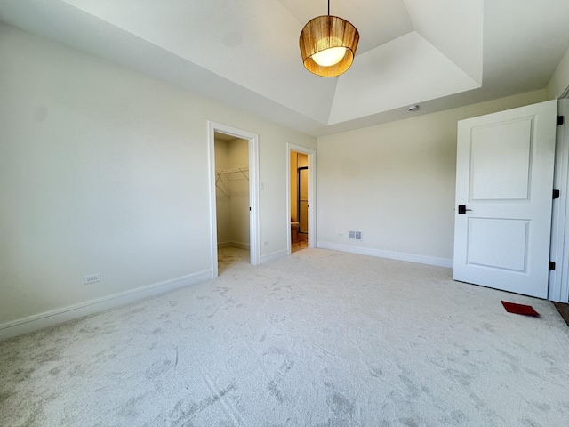 unfurnished bedroom featuring light carpet, a spacious closet, baseboards, a tray ceiling, and a closet
