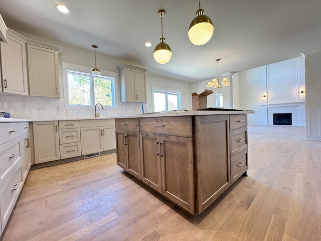 kitchen with a fireplace, decorative backsplash, a sink, light wood-style flooring, and recessed lighting