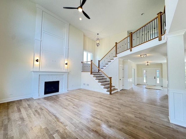 unfurnished living room featuring ceiling fan, healthy amount of natural light, stairs, light wood finished floors, and a high ceiling