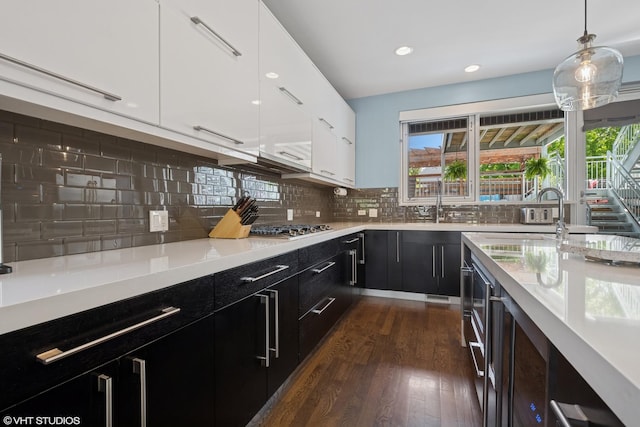 kitchen featuring dark cabinets, dark wood-style flooring, light countertops, stainless steel gas stovetop, and white cabinetry