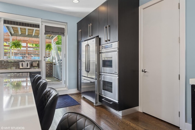 kitchen featuring appliances with stainless steel finishes, dark wood-type flooring, recessed lighting, dark cabinetry, and baseboards