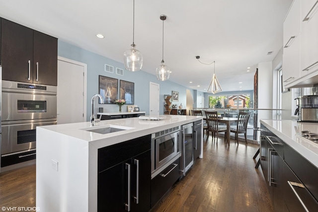 kitchen featuring a sink, appliances with stainless steel finishes, light countertops, wine cooler, and recessed lighting