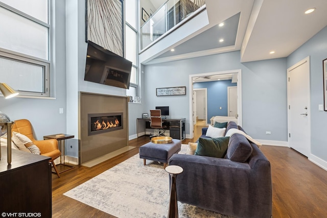 living room featuring dark wood finished floors, a large fireplace, a high ceiling, baseboards, and recessed lighting