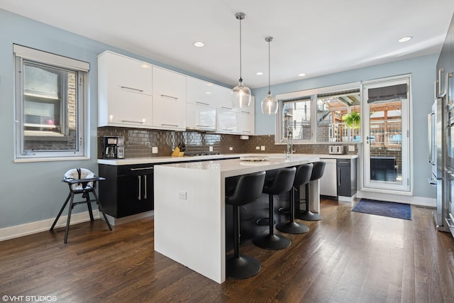 kitchen featuring dishwasher, light countertops, a breakfast bar, a center island, and tasteful backsplash