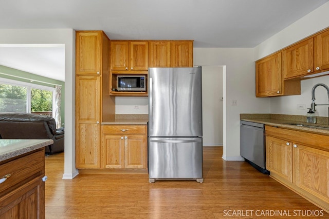 kitchen with appliances with stainless steel finishes, a sink, light wood finished floors, baseboards, and brown cabinets