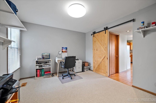 office area with light carpet, a barn door, and baseboards