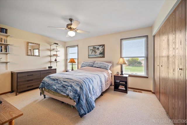 bedroom featuring a closet, light colored carpet, baseboards, and a ceiling fan