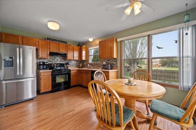 kitchen with stainless steel fridge, black gas range, under cabinet range hood, backsplash, and light wood finished floors