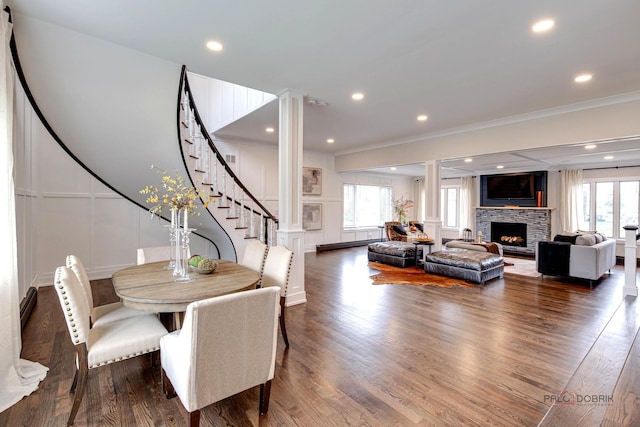 dining space featuring crown molding, ornate columns, a decorative wall, a lit fireplace, and wood finished floors