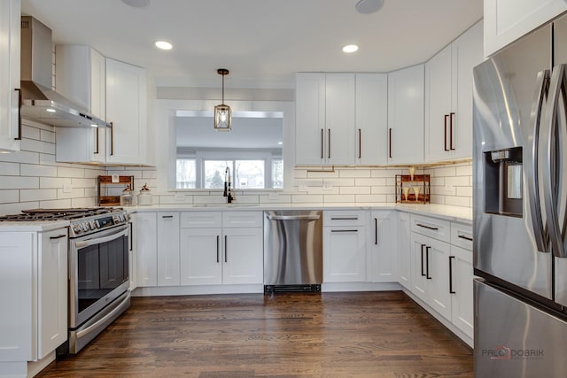 kitchen featuring appliances with stainless steel finishes, a sink, wall chimney exhaust hood, white cabinets, and backsplash