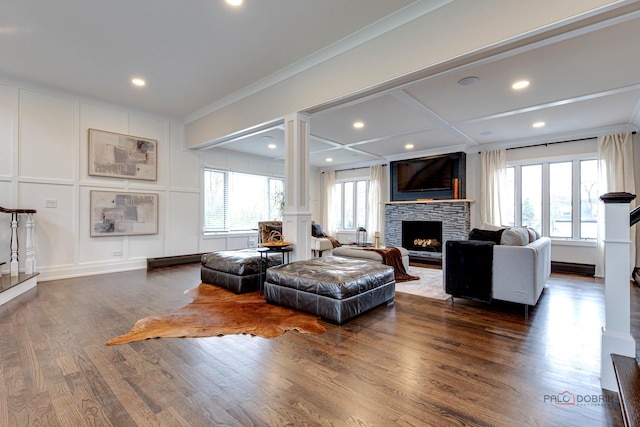 living room with plenty of natural light, a fireplace, a decorative wall, dark wood finished floors, and crown molding