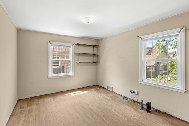 empty room with wood finished floors, baseboards, and ornamental molding