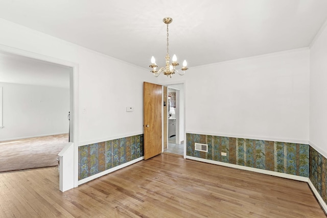 unfurnished dining area featuring wood finished floors, ornamental molding, a chandelier, wallpapered walls, and baseboards