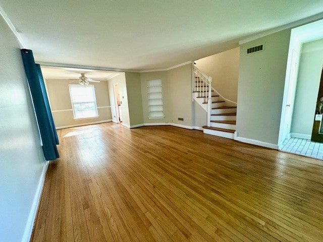 unfurnished living room with wood finished floors, baseboards, stairway, crown molding, and a ceiling fan