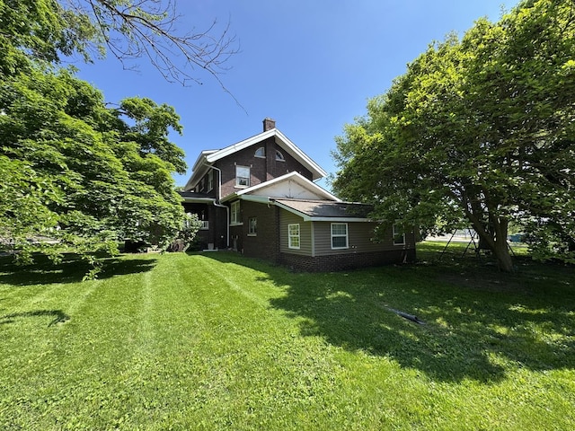 view of side of property featuring a yard, a chimney, and brick siding