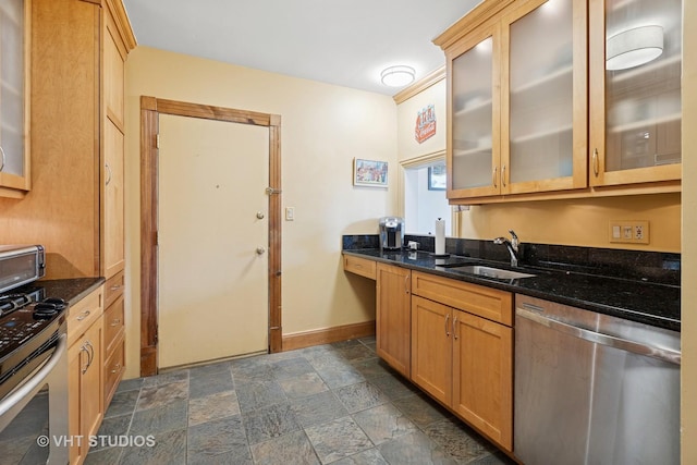 kitchen with appliances with stainless steel finishes, a sink, dark stone finish flooring, baseboards, and dark stone counters