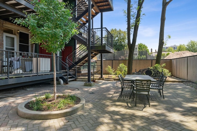 view of patio with outdoor dining space, fence, and stairs