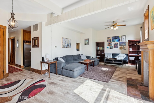living area featuring light wood finished floors, beamed ceiling, a ceiling fan, a chandelier, and baseboards