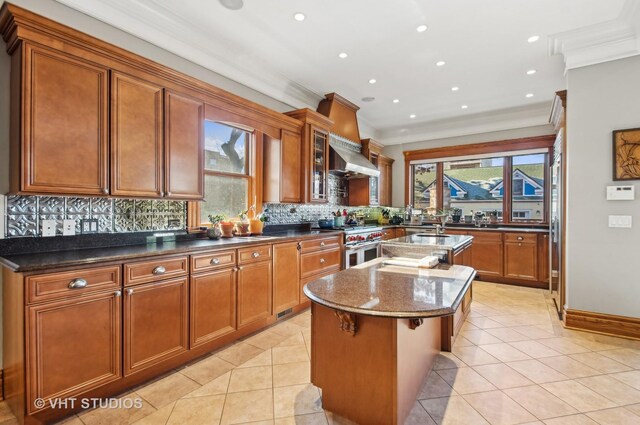 4752 N Beacon St, Chicago, IL 60613 - kitchen with range with two ovens, ornamental molding, an island with sink, light tile patterned floors, and brown cabinets